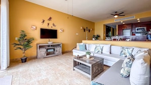 A living room with a sofa, coffee table, TV, and a potted plant. - 1BR Oceanview Condo w/pool (Isla Mujeres)