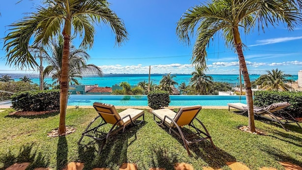A poolside area with two lounge chairs, a clear view of the ocean, and a well-maintained lawn. - 1BR Oceanview Condo w/pool (Isla Mujeres)