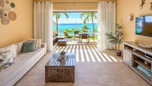 A living room with a sofa, coffee table, and TV, leading to a balcony with a view of the ocean. - 1BR Oceanview Condo w/pool (Isla Mujeres)