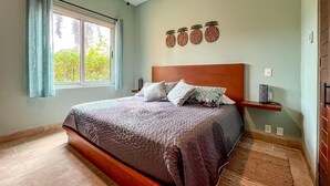 A bedroom with a large bed, a window with curtains, a headboard, and wall-mounted decorations. - 1BR Oceanview Condo w/pool (Isla Mujeres)