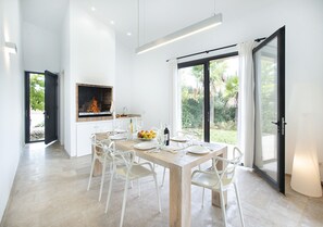 Un comedor moderno con una mesa de madera, sillas blancas y una chimenea empotrada.