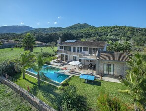 Una casa de dos plantas con piscina, mobiliario exterior y vistas a las colinas circundantes.