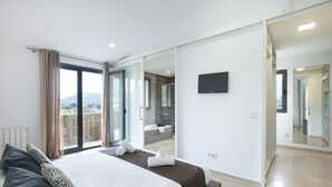 Ein modernes Schlafzimmer mit einem großen Bett, einer Glastür zum Balkon und einem durch eine offene Tür sichtbaren Badezimmer.
