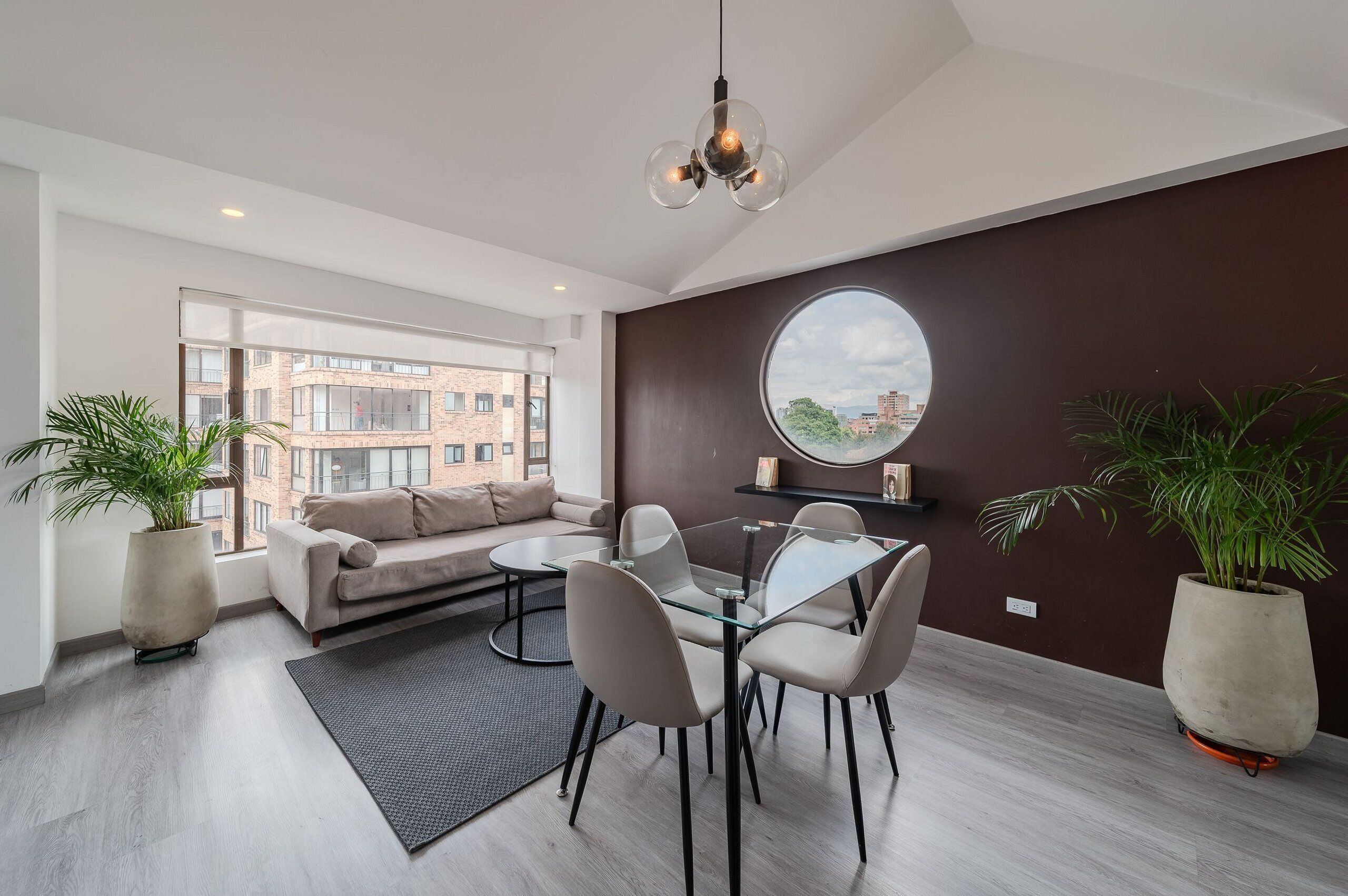 A modern living room with a glass table, beige sofa, and potted plants.