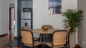 A dining area with a wooden table and four chairs, a large potted plant, and a framed picture on the wall.