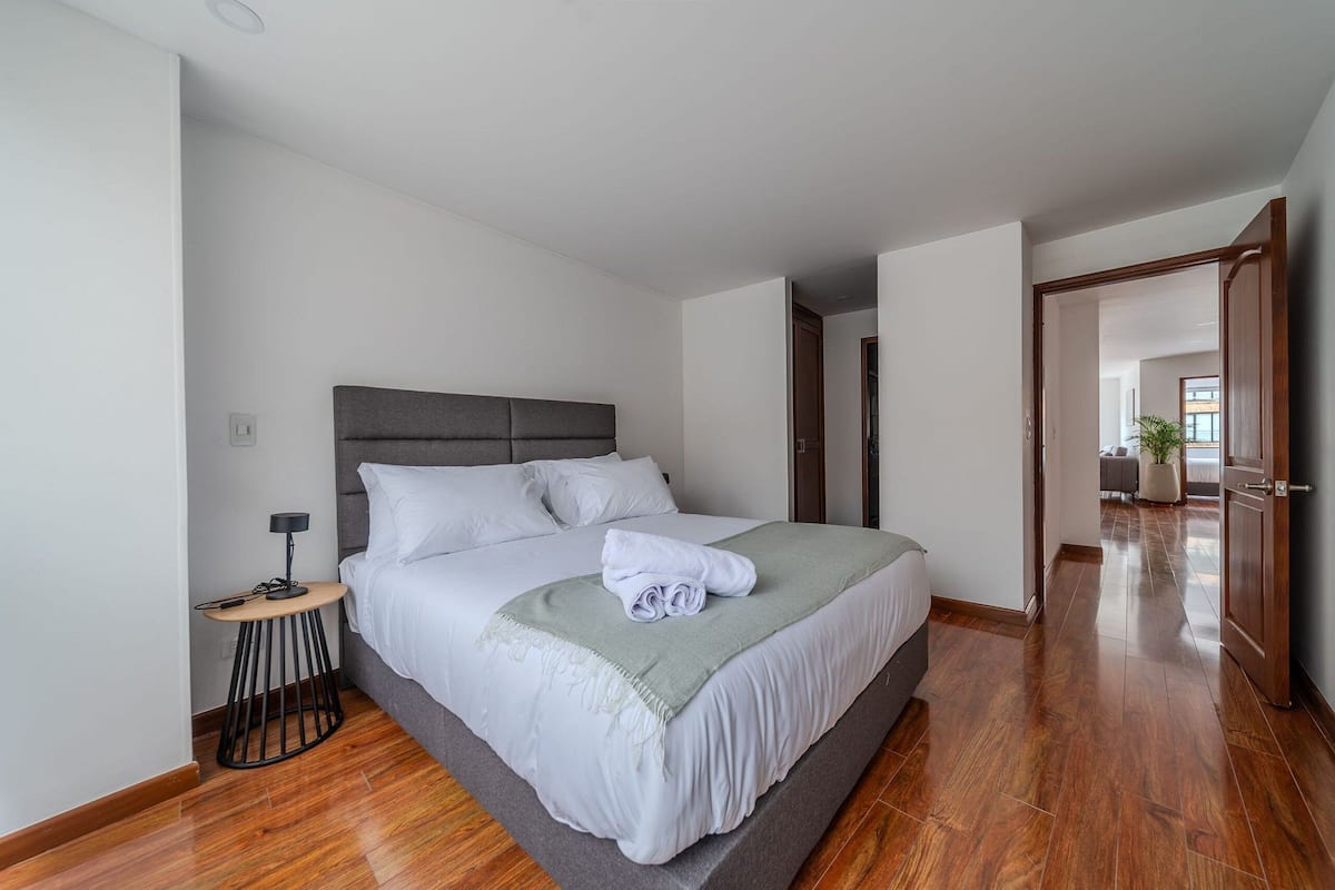 Une chambre moderne avec un grand lit, une table de chevet et une vue sur une autre pièce.
