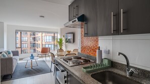 A modern kitchen with dark cabinets, a built-in stove, and a large window offering a view of the cityscape. - 10.73 Flats x Ahead (Bogotá)
