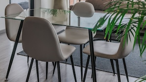 A modern dining area with a glass table, four chairs, a potted plant, and a city view through large windows. - 10.73 Flats x Ahead (Bogotá)
