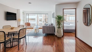 A modern living room with a dining area, a sofa, a TV, and a large window. - 10.73 Flats x Ahead (Bogotá)