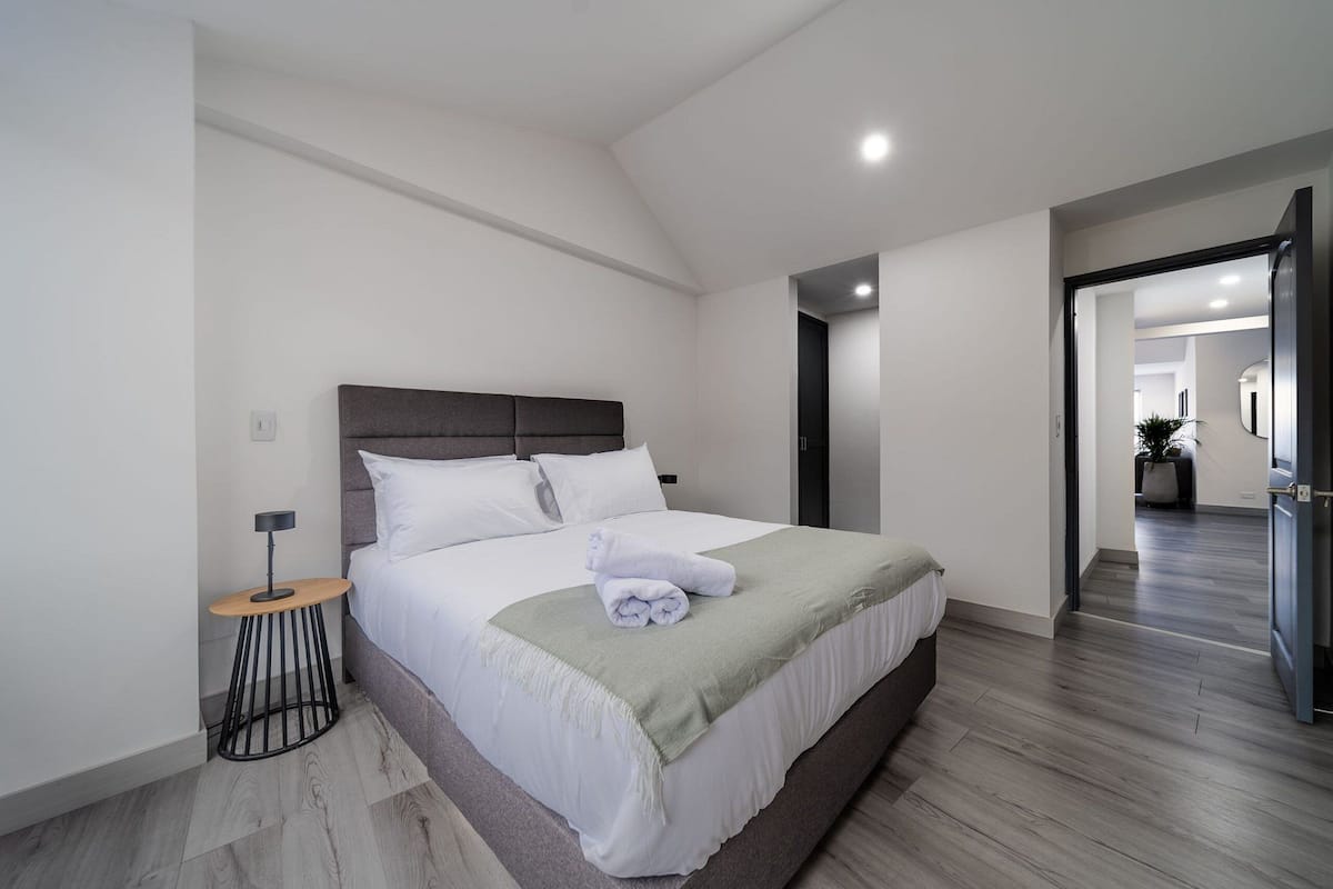 Une chambre moderne avec un grand lit, une table de chevet et un petit tabouret.