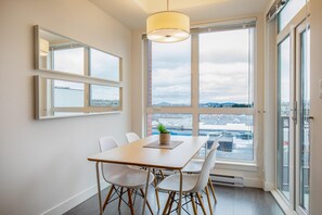 A modern dining area with a large window, a table with chairs, and a hanging light fixture. - Bright and Trendy Heritage Suite in Old Town (Victoria Central British Columbia Provincial Government)