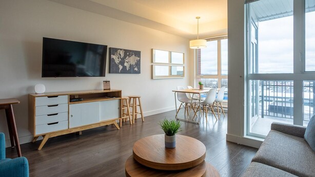 Ein modernes Wohnzimmer mit Flachbildfernseher, einer Holzkommode, einem runden Couchtisch mit Pflanze, einer Couch und einem Essbereich mit Stühlen und Tisch.