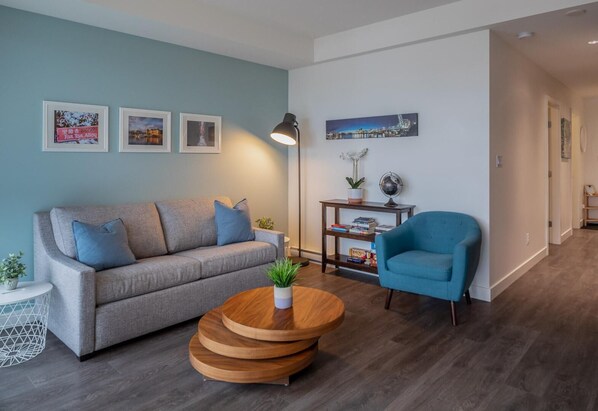 Un salon avec un canapé gris, un fauteuil bleu, une table basse en bois et une petite table d’appoint sur laquelle est posée une plante.