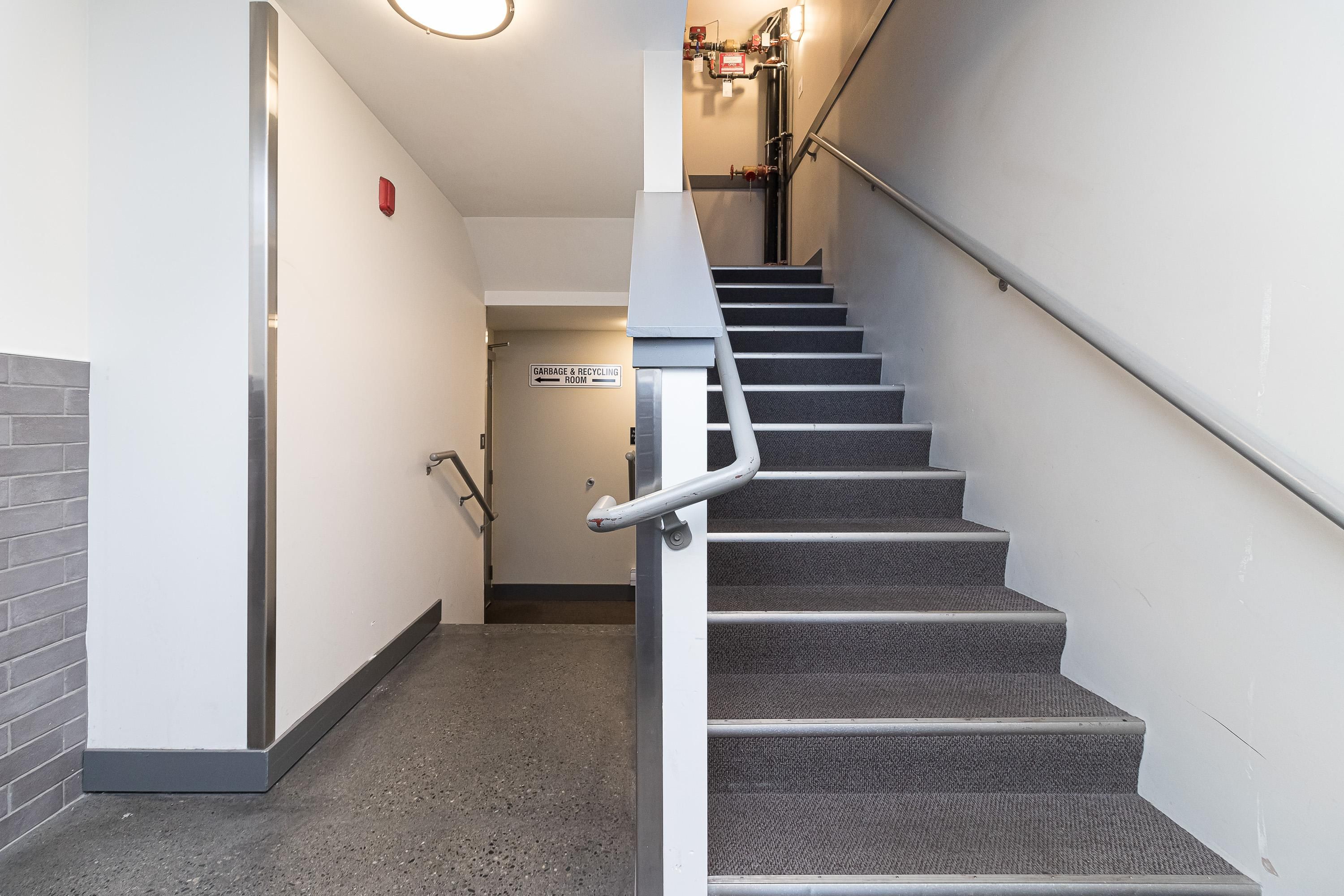 Eine Treppe mit Handlauf, Teppichstufen und einem an der Wand befestigten Schild, das einen Müll- und Recyclingraum kennzeichnet.