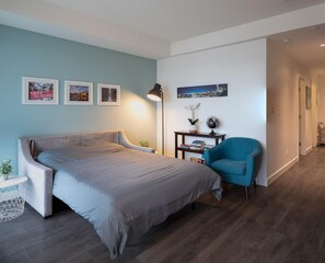 Une chambre à coucher moderne avec un grand lit, un fauteuil bleu et une petite table de chevet avec une lampe.