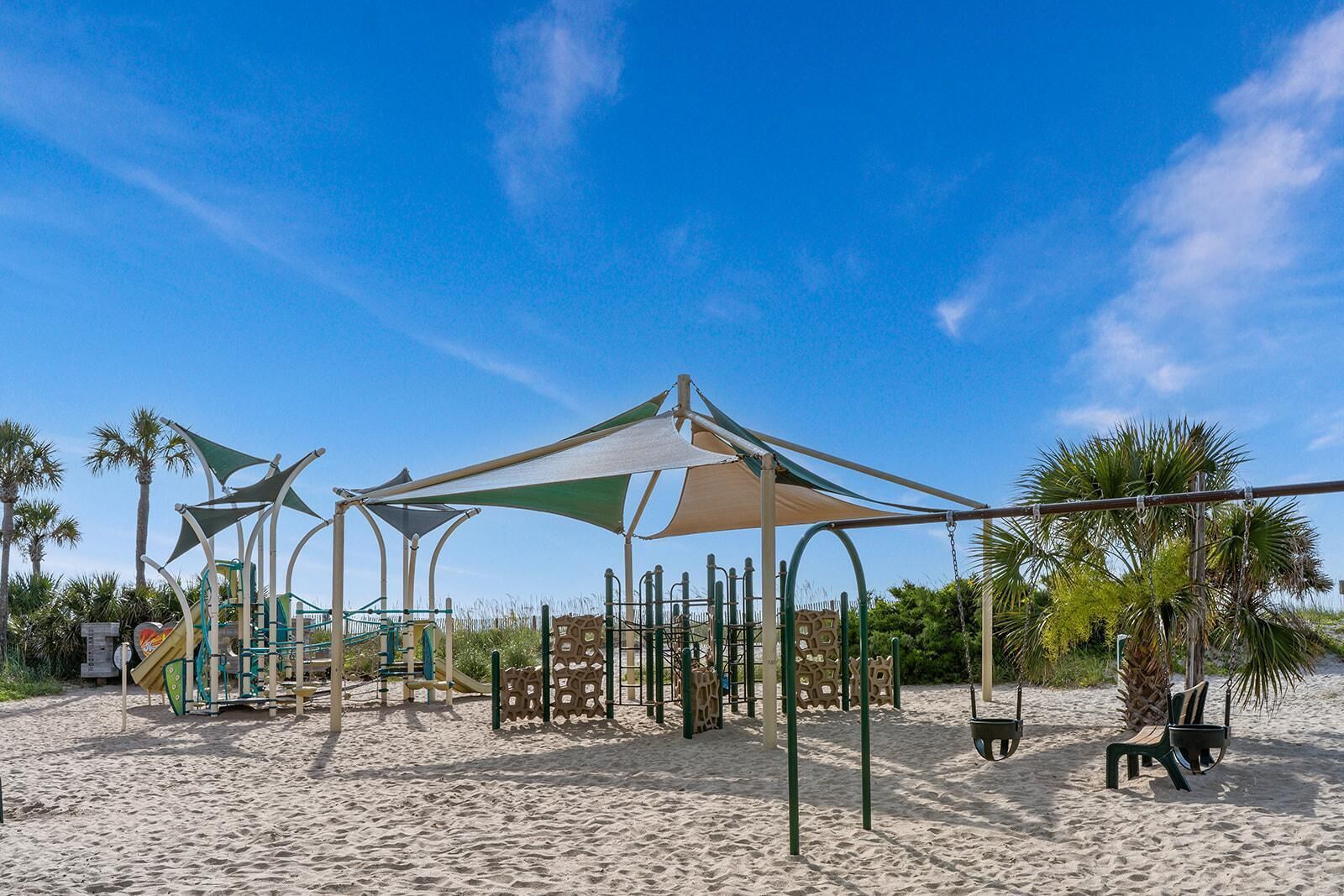 A beach playground with play structures, shaded areas, and palm trees.
