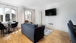 Ein modernes Wohnzimmer mit einer Couch, einem Esstisch mit Stühlen und einem an der Wand befestigten Flachbildfernseher.