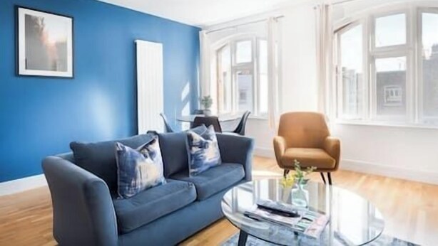 Ein modernes Wohnzimmer mit blauer Wand, einem Sofa, einem Couchtisch und einem Fenster.