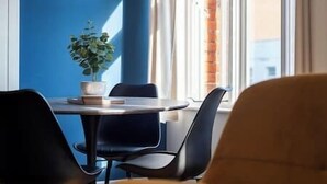 Ein Essbereich mit Tisch und Stühlen, einem Blumentopf und Blick auf ein Gebäude durch das Fenster.