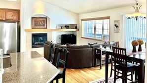 A modern kitchen with a built-in oven, a dining area with a table and chairs, a large L-shaped sofa, and a fireplace.