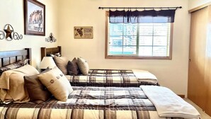 A bedroom with two beds, a ceiling fan, a window with blinds, and wall decorations.