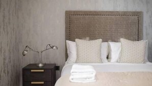 A neatly made bed with a textured headboard, a bedside lamp, and a dark wooden nightstand with drawers.