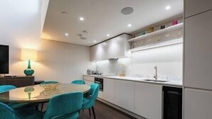 A modern kitchen with white cabinets, a round dining table, teal chairs, and a built-in oven.