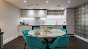 A modern kitchen with white cabinets, a marble backsplash, and a round dining table with teal chairs.