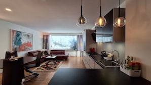 A modern living room with a sofa, dining table, and kitchen area with a sink and cabinets. - Panorama App 1B Zell am See (Zell am See)