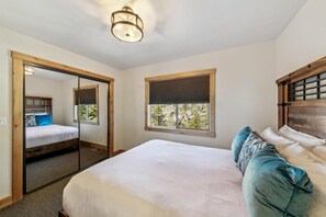 A bedroom with a large bed, a mirror, a window with blinds, and a ceiling light fixture.
