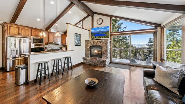 A spacious living area with a stone fireplace, wooden beams, and large windows offering a view of the outdoors. - Top of Kingsbury View Home 7BR,4BA,Spa, 5 To Ski (Stateline)
