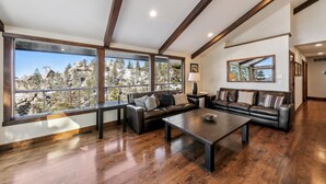 A spacious living room with large windows, a leather sofa, a coffee table, and wooden floors. - Top of Kingsbury View Home 7BR,4BA,Spa, 5 To Ski (Stateline)