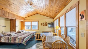A cabin with two beds, a dining table, chairs, a television, and a window with blinds.