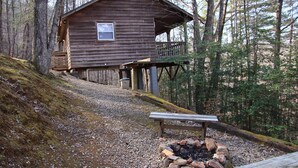 A wooden cabin with a deck, surrounded by trees.