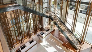 A modern interior with a glass staircase, wooden railings, and a view of the street outside.