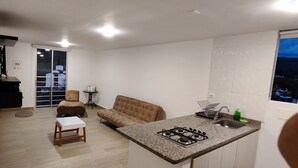 A compact kitchen with a gas stove, a small dining table, a sofa, and a sliding door leading to a balcony.