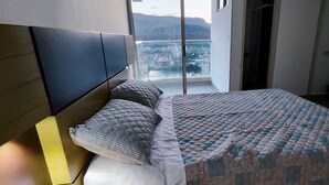 A bedroom with a bed, a headboard, and a window with a city view.