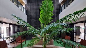 Ein zeitgemäßes Innen-Atrium mit einem zentralen Pflanzenbeet, in dessen Mittel eine hohe Zimmerpalme steht, umgeben von Sitzbereichen und einer hohen Decke mit schwarzen Fliesenwänden.