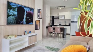 Ein modernes Wohnzimmer mit einem Flachbildfernseher, einer weißen Unterhaltungseinheit und einem Sofa mit einem orangefarbenen Kissen.