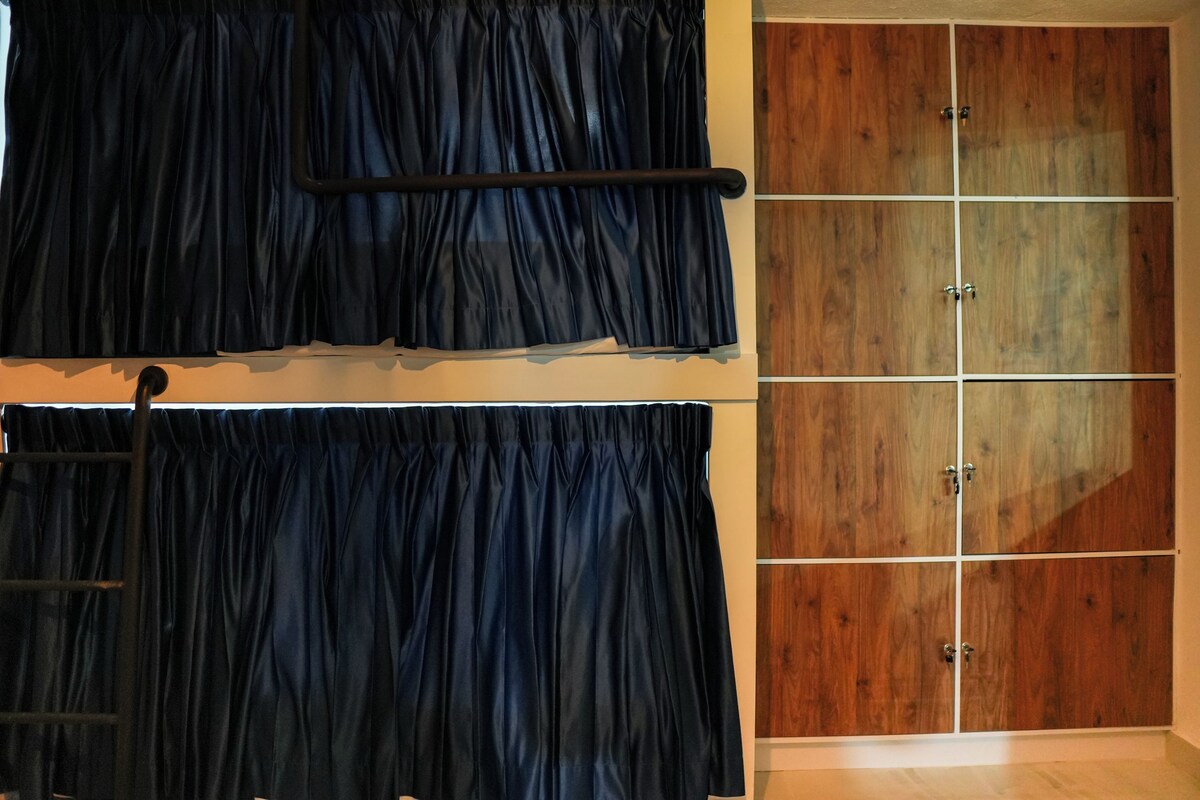 A room with two sets of dark curtains, a wooden wardrobe with multiple compartments, and a metal ladder.