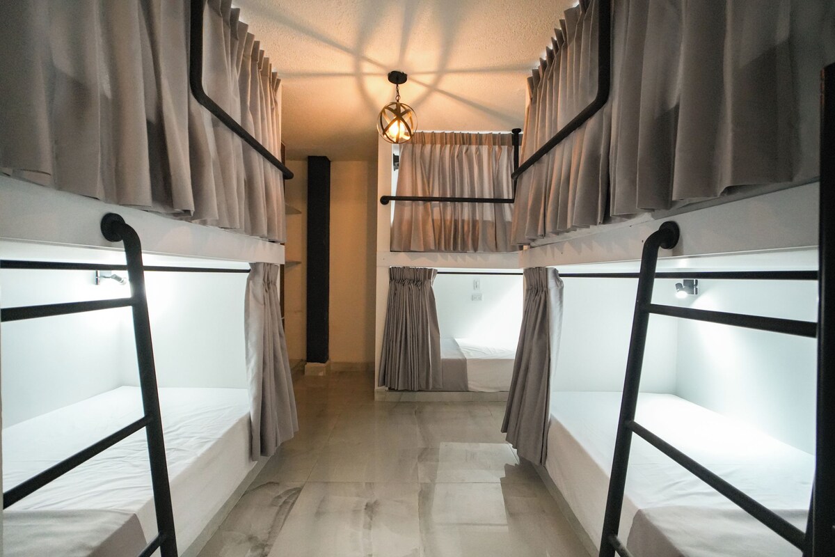 A dormitory-style room with bunk beds, curtains, and a hanging light fixture.