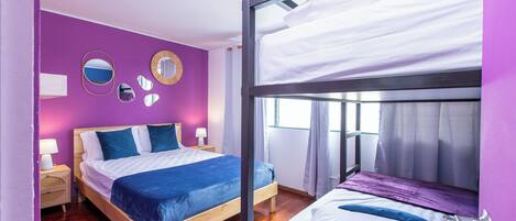 A room with a bunk bed, a single bed, wooden flooring, and purple walls.