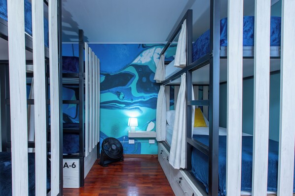 Um corredor com beliches, um ventilador e um mural na parede.