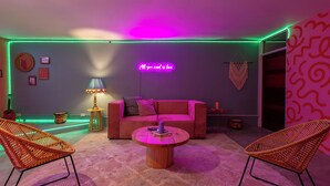 A modern living room with a pink sofa, two wicker chairs, a coffee table, and a neon sign. - Casa Zafiro B&B (San Pedro)