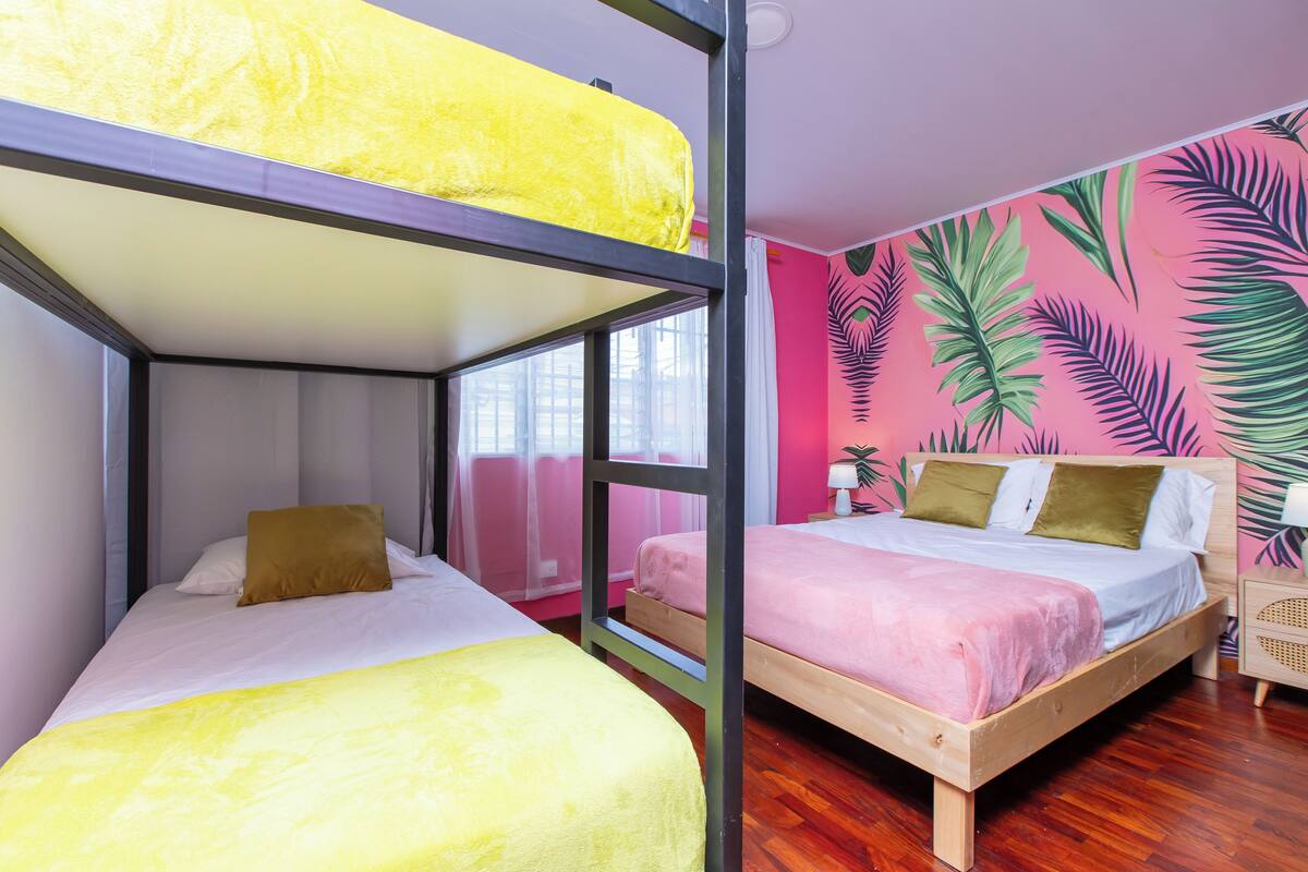 Een kamer met stapelbedden, een bed met een roze deken en een muur met een tropisch bladpatroon.