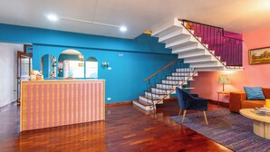 A modern living room with a wooden floor, a blue accent wall, a staircase with a unique railing design, and a seating area with a blue chair and a small table. - Casa Zafiro B&B (San Pedro)