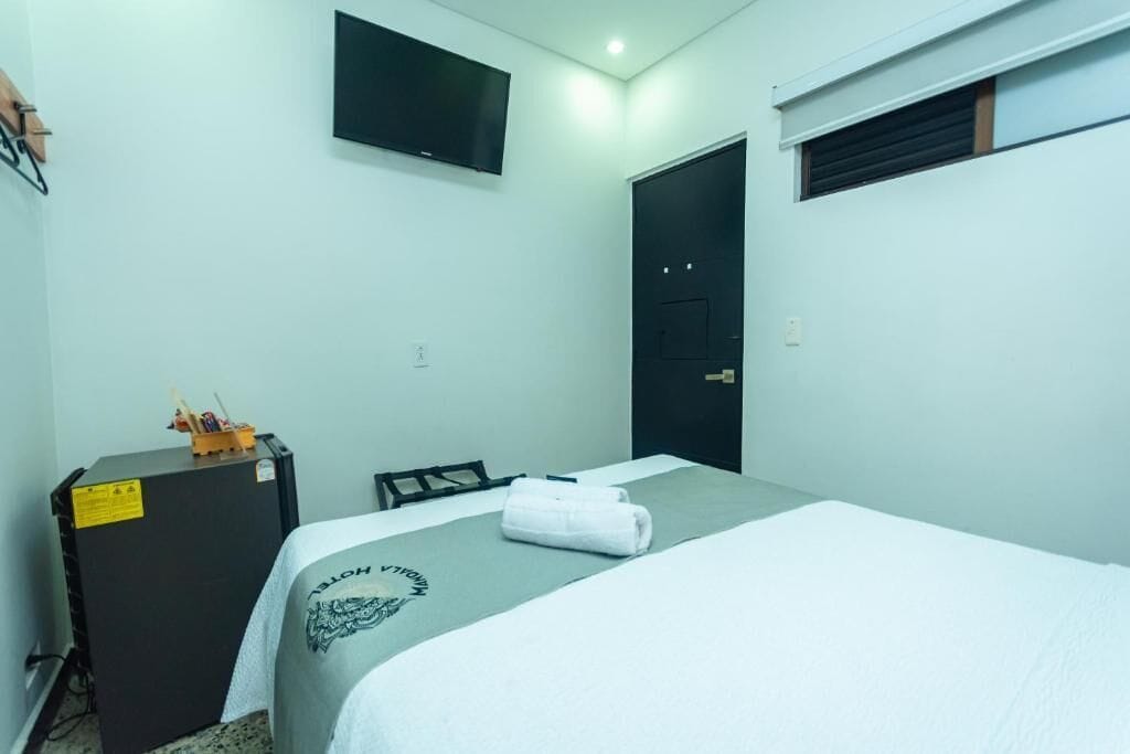 Una habitación de hotel con una cama, un escritorio, un televisor fijado a la pared y una puerta.