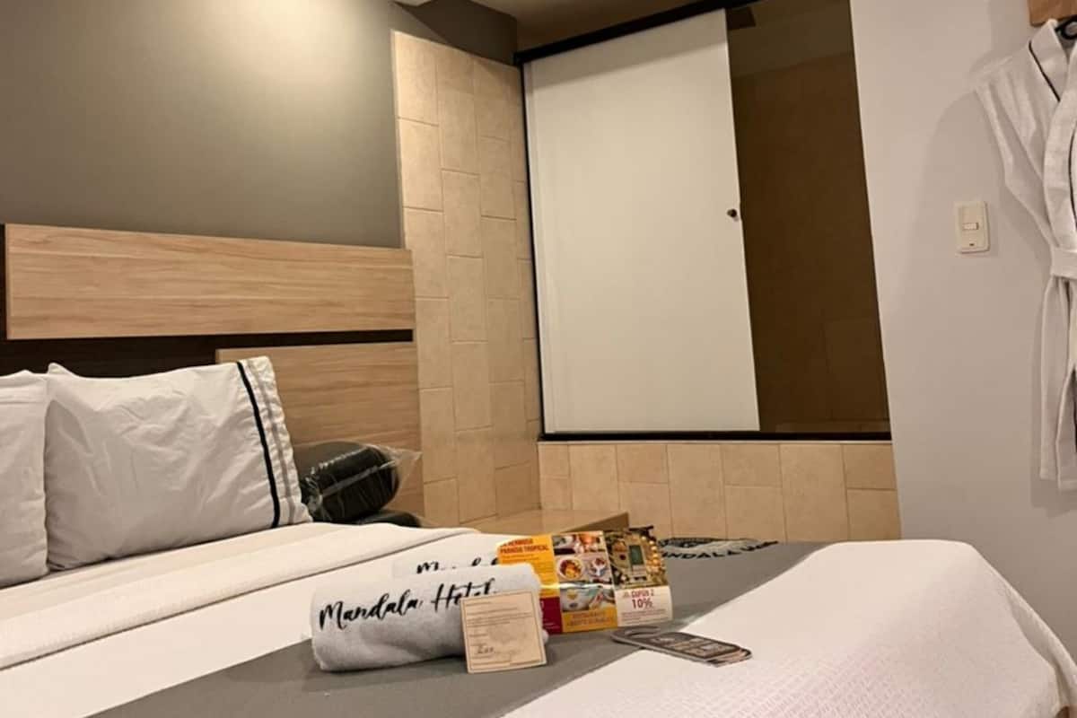 A hotel room with a bed, a robe hanging on the wall, and a fan.