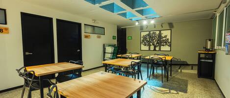 A classroom with tables and chairs, a projector, and a window with a tree painting.
