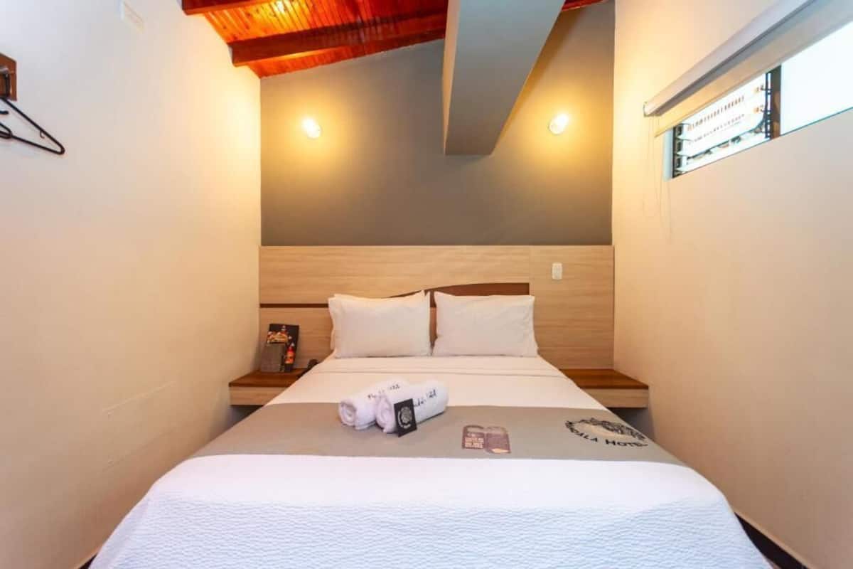 A hotel room with a wooden headboard, a bed with white bedding, a small bedside table, and a window with a view.